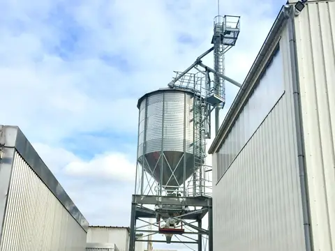 Silo en hauteur entre deux bâtiments industriels, sous un ciel nuageux