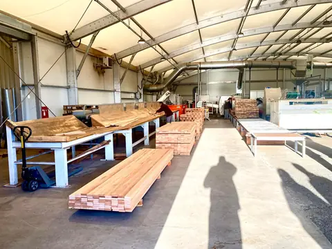 Atelier de production sous charpente métallique, avec bois débité sur un chariot