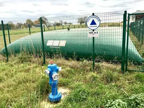 Réserve d’eau souple verte, clôturée et signalée, avec un poteau d’incendie bleu au premier plan