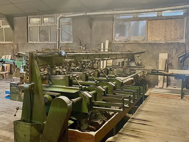 Ligne de machines dans un atelier de transformation du bois, sol couvert de sciure